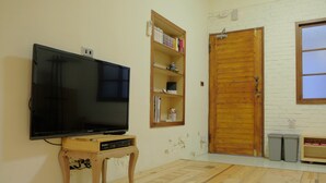 Ein Wohnzimmer mit einem Flachbildfernseher auf einem Holzboden, einem Bücherregal, einer Holztür und einem Fenster.