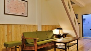 Ein gemütliches Zimmer mit Holzboden, einem grünen Sofa, einem Holztisch und einer Lampe.