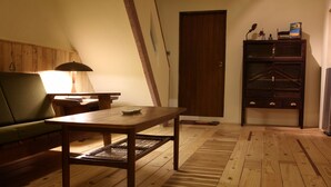 Ein Zimmer mit Holzboden, einem grünen Sofa, einem Holztisch, einer Lampe und einem Holzkasten.