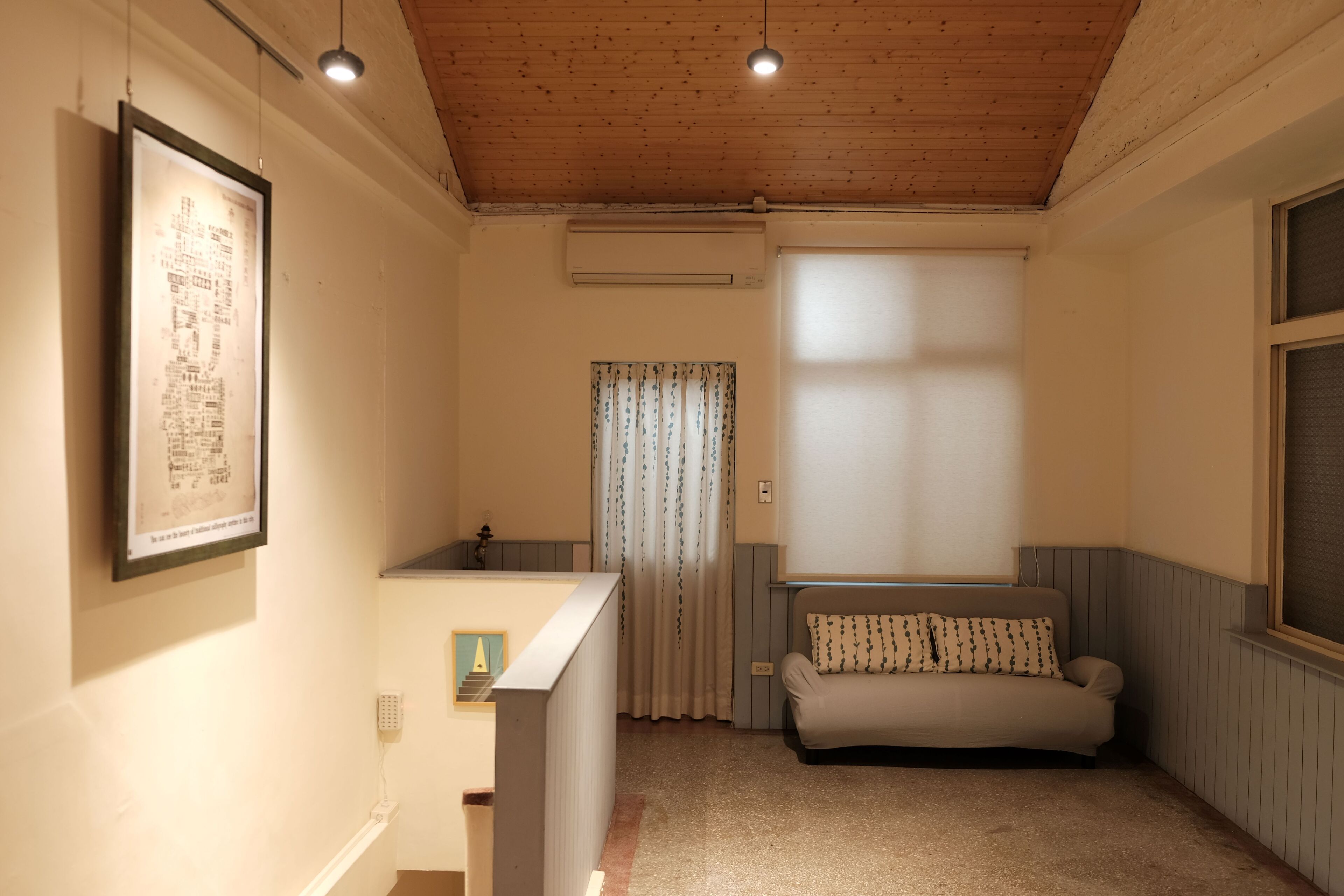 A room with a wooden ceiling, a sofa, a framed picture, and a window with curtains.