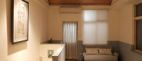 A room with a wooden ceiling, a sofa, a framed picture, and a window with curtains.