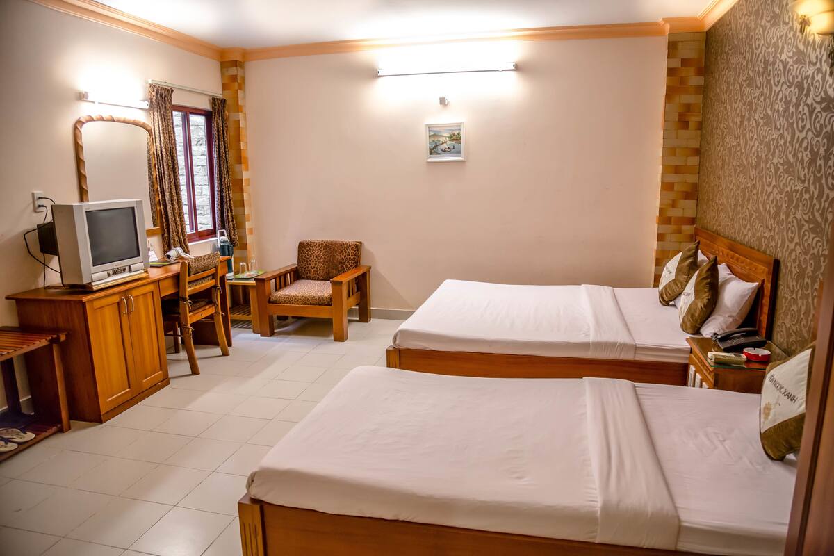 Ein Hotelzimmer mit zwei Betten, einem Schreibtisch mit Fernseher, einem Sessel und einem kleinen Tisch mit Telefon.