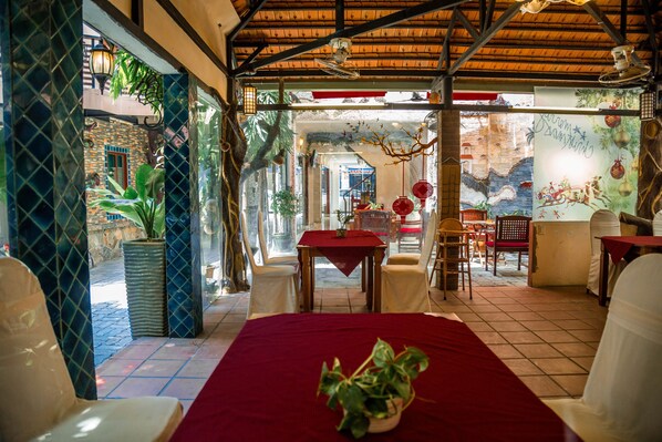A room with a red table, white chairs, and a potted plant. There is a window with a view of the outside.