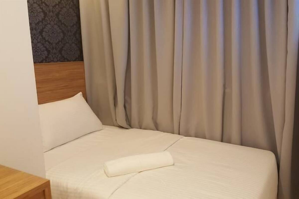 Ein ordentlich bezogenes Bett mit einem weißen Kopfkissen und einem aufgerollten weißen Handtuch.