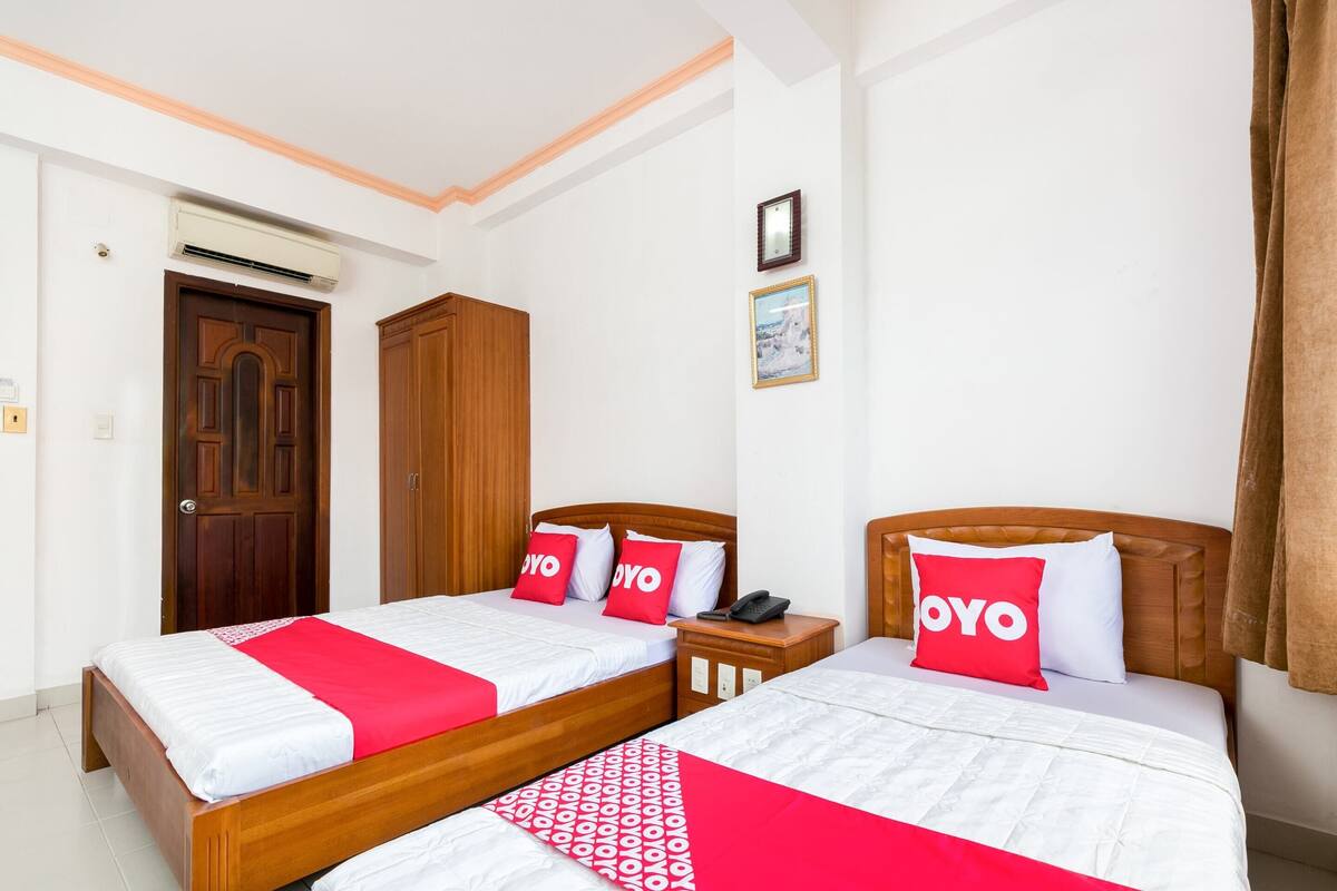 Ein Hotelzimmer mit zwei Betten, jeweils mit einem hölzernen Kopfstück, weißer Bettwäsche und roten Kissen mit 