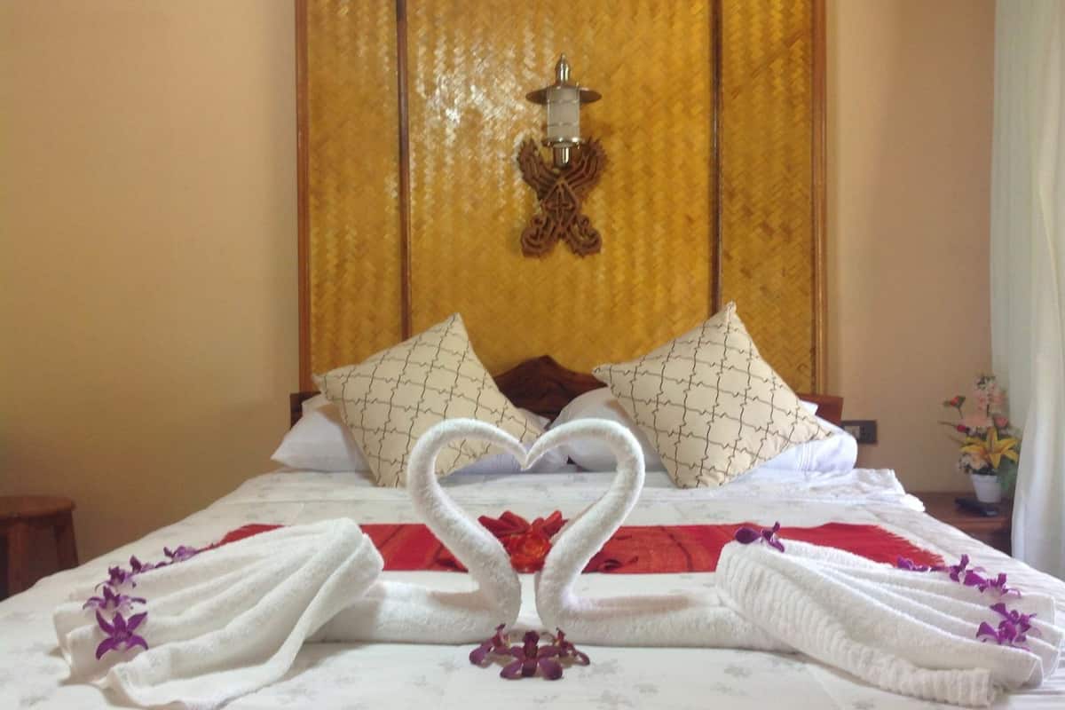 A hotel room with a bed, pillows, a decorative wall, and a nightstand with a vase of flowers.
