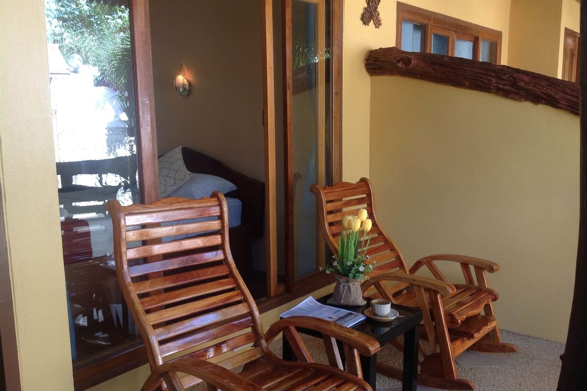 A cozy seating area with wooden chairs and a small table, a mirror, and a decorative wall piece.