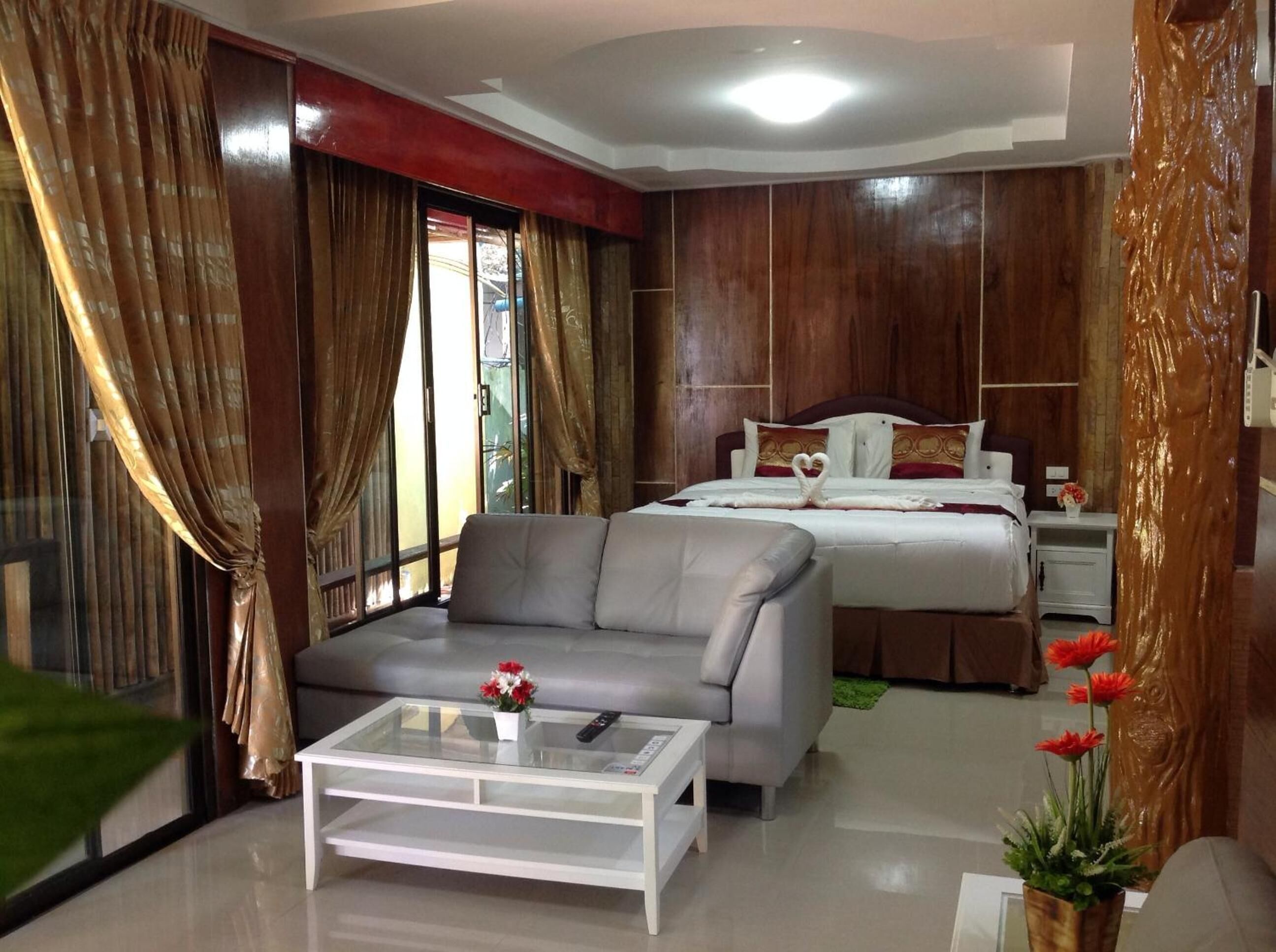A modern hotel room with a sofa, a bed with heart-shaped pillows, a nightstand, and a glass coffee table.