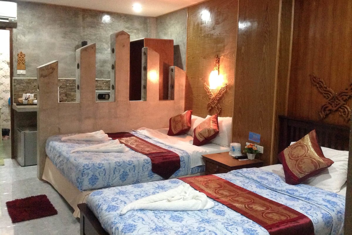 A hotel room with two beds, a wooden headboard, a mirror, and a small table with a vase.