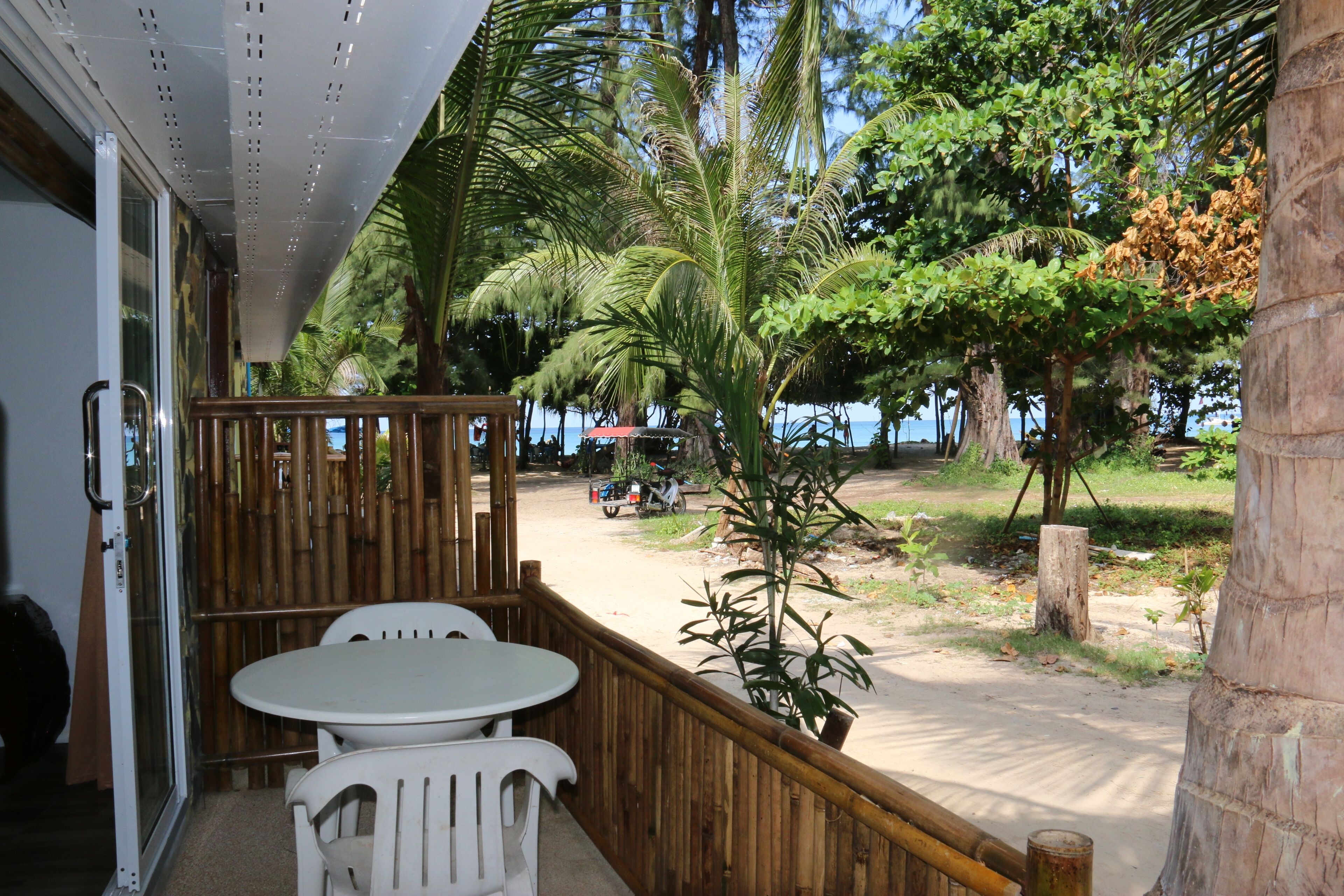 A covered outdoor seating area with a table and chairs, overlooking a sandy beach and palm trees.