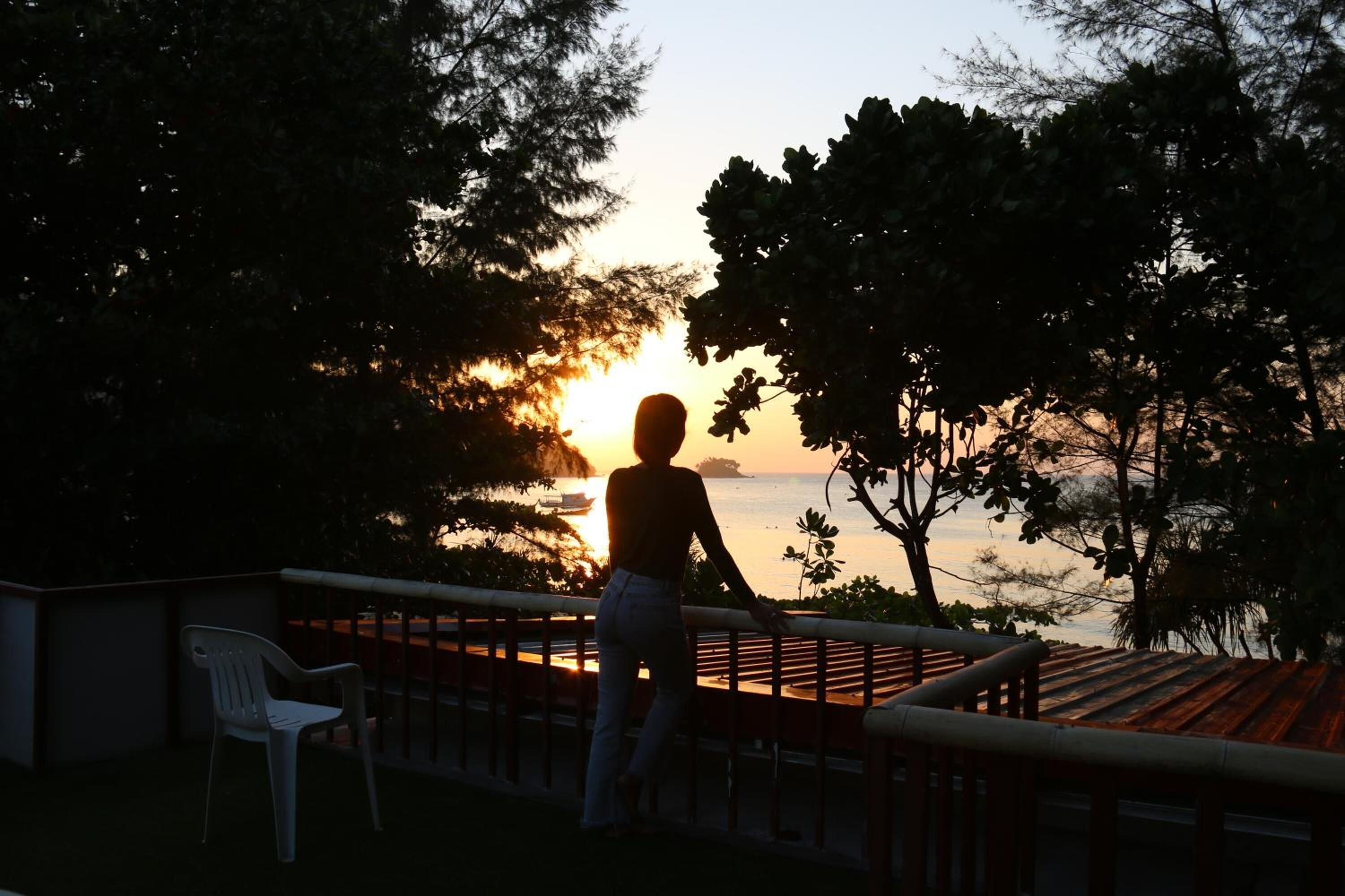 A person standing on a balcony overlooking a sunset.