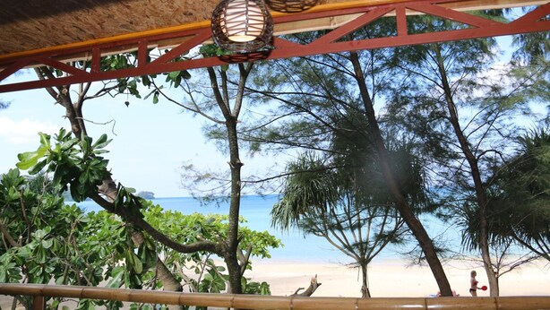 A beach view with a thatched roof structure, hanging wicker lamps, and dense foliage.