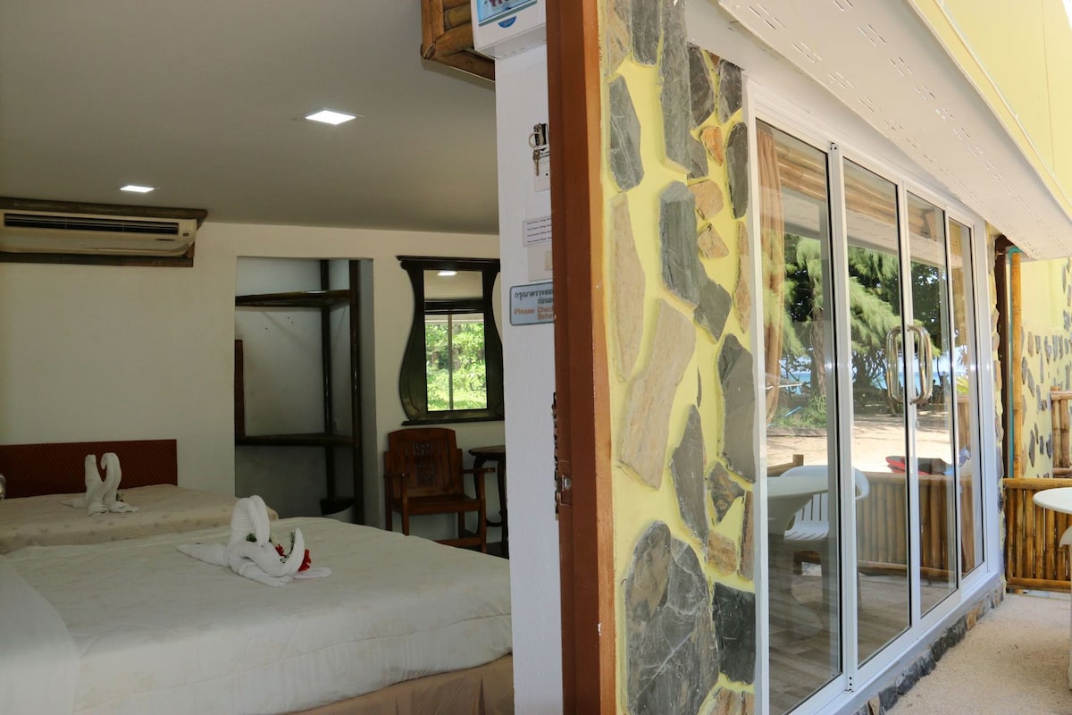 A hotel room with a bed, a chair, a table, and a view through a glass door.
