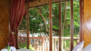 A room with a bed, a window with a view of trees, and a wooden railing outside.