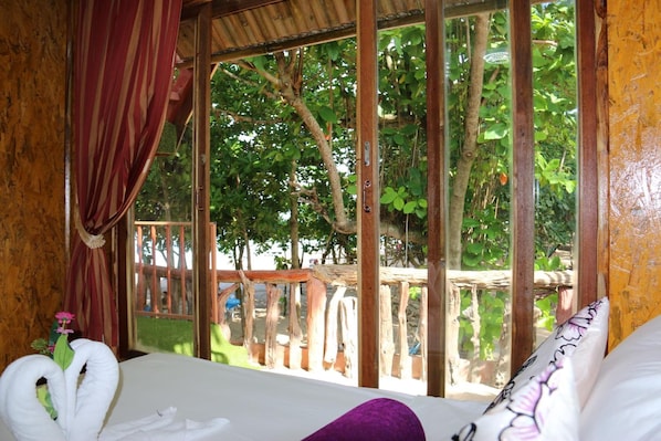 A room with a bed, a window with a view of trees, and a wooden railing outside.