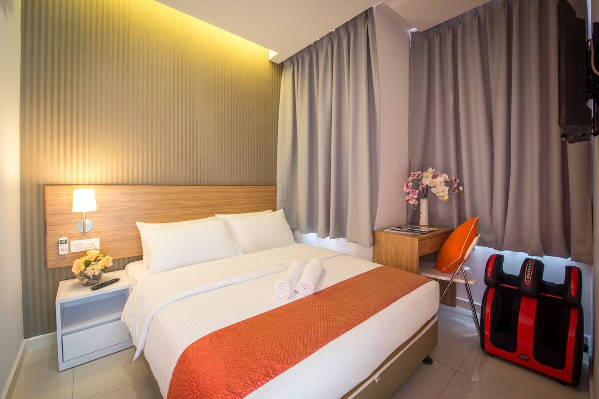 Ein Hotelzimmer mit Bett, Nachttisch mit Lampe, Massagesessel und Wand-Fernseher.