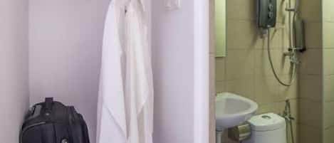 A bathroom with a shower, toilet, and sink. There is a wooden shelf with towels and a suitcase.