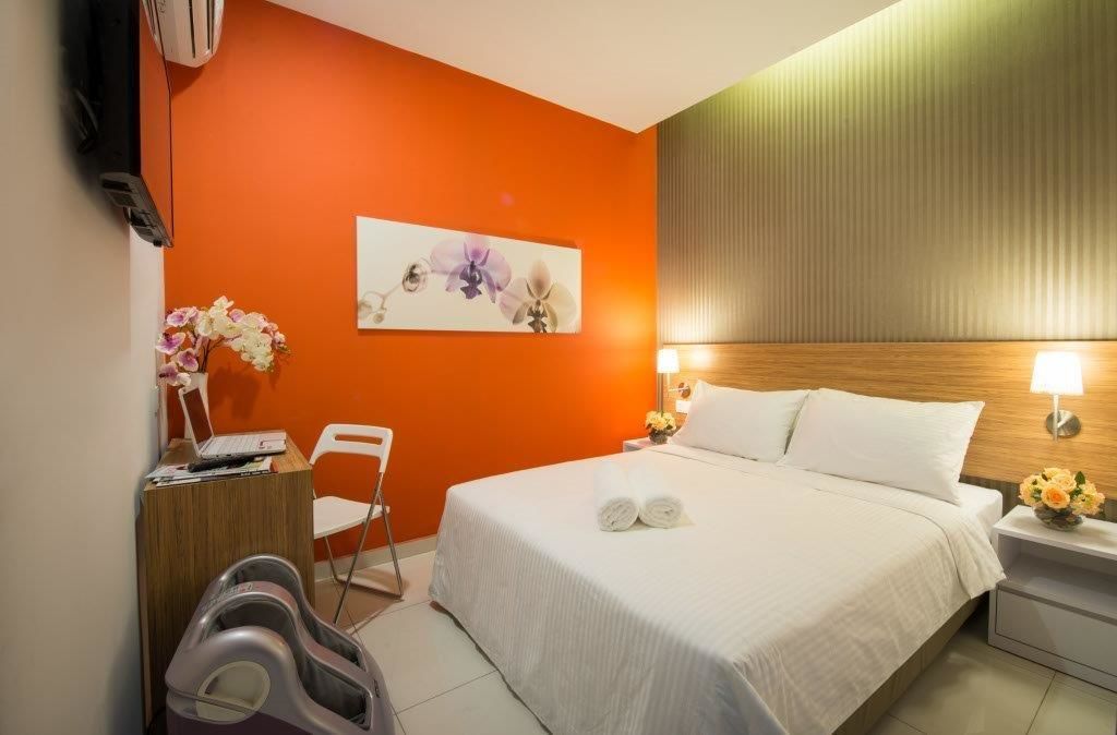 A hotel room with a bed, a desk with a laptop, a chair, and a massage chair.