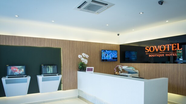 A modern hotel reception area with a reception desk, two monitors, and a television.