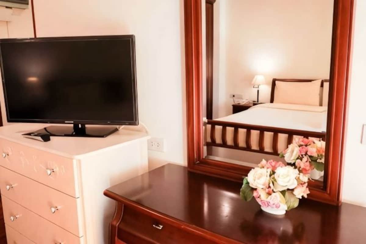A hotel room with a television on a dresser, a bed with a wooden headboard, and a vase with flowers on a dresser.