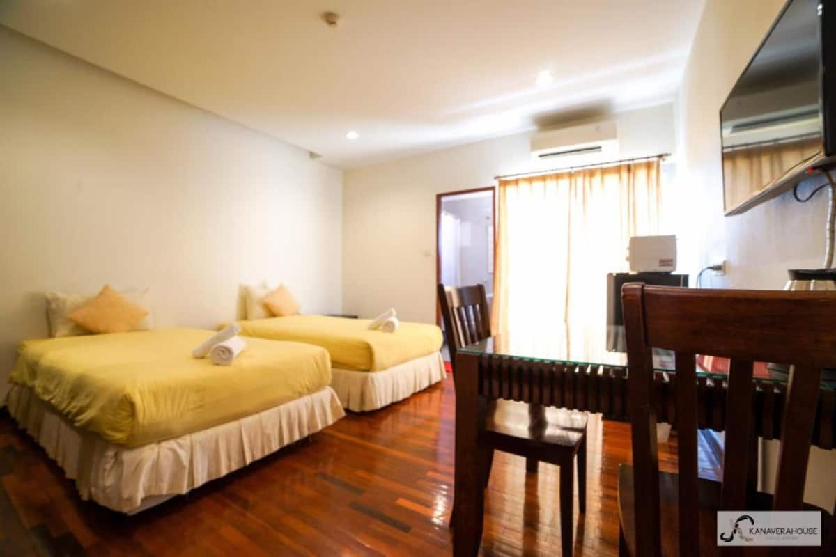 Habitació d'hotel amb dos llits, un terra de fusta, un televisor i un aparell d'aire condicionat.
