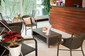 Un espace d’accueil avec des meubles en osier, un comptoir de réception et une table basse agrémentée d’un arrangement floral.