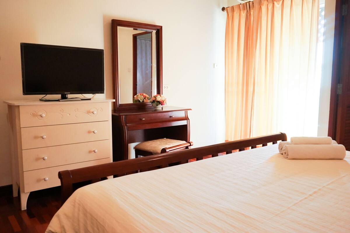 Habitació d'hotel ben ordenada amb un llit, un televisor sobre una petita taula, un mirall i una finestra amb cortines.