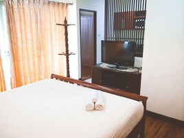 A hotel room with a bed, a television on a wooden stand, and a curtain with a floral pattern.