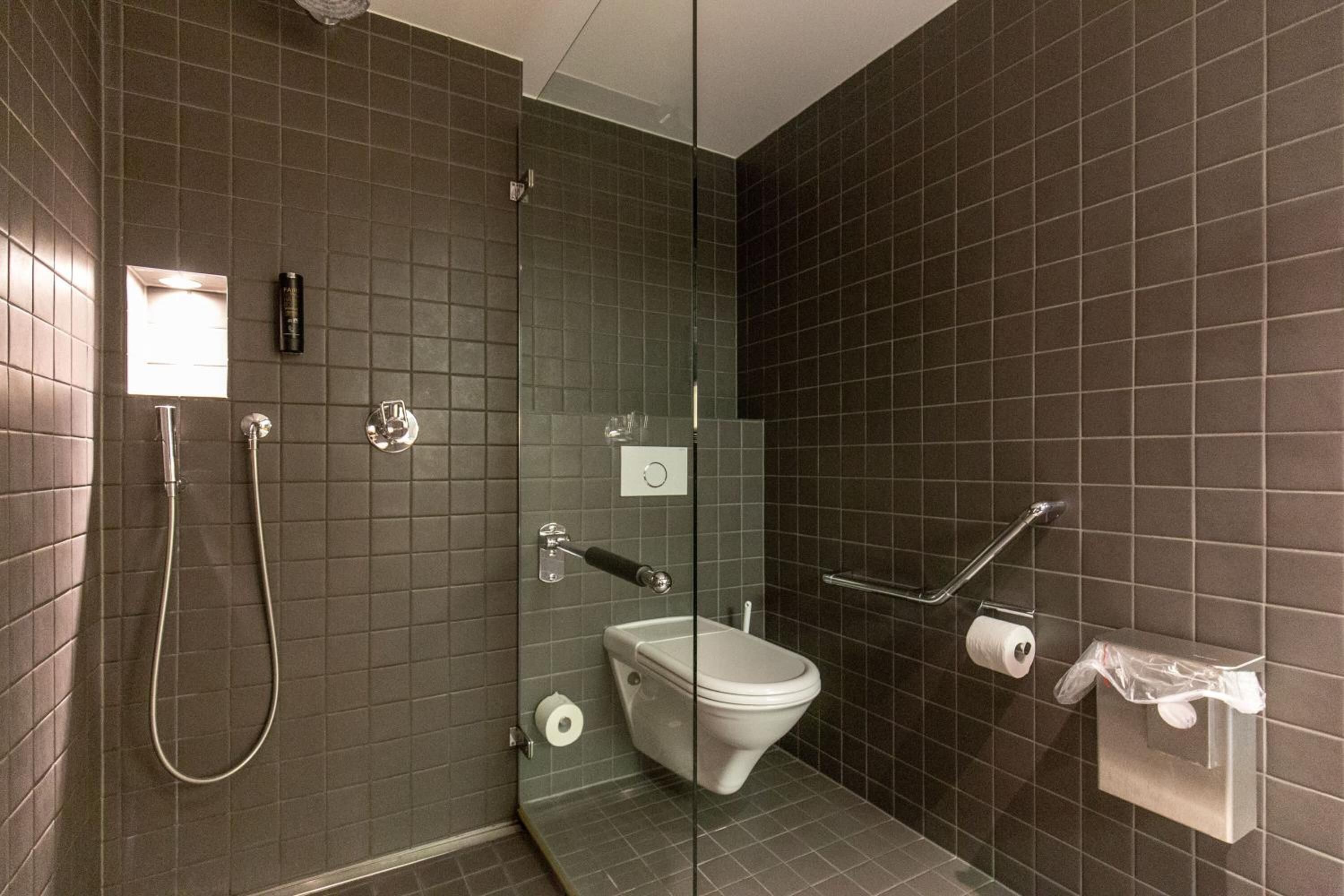 Une salle de bain moderne dotée d’une douche à parois de verre, de toilettes et d’un sèche-mains.