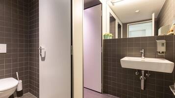 Ein modernes Badezimmer mit dunkel gefliesten Wänden, einer weißen Toilette und einem integrierten Waschbecken mit Spiegel darüber.