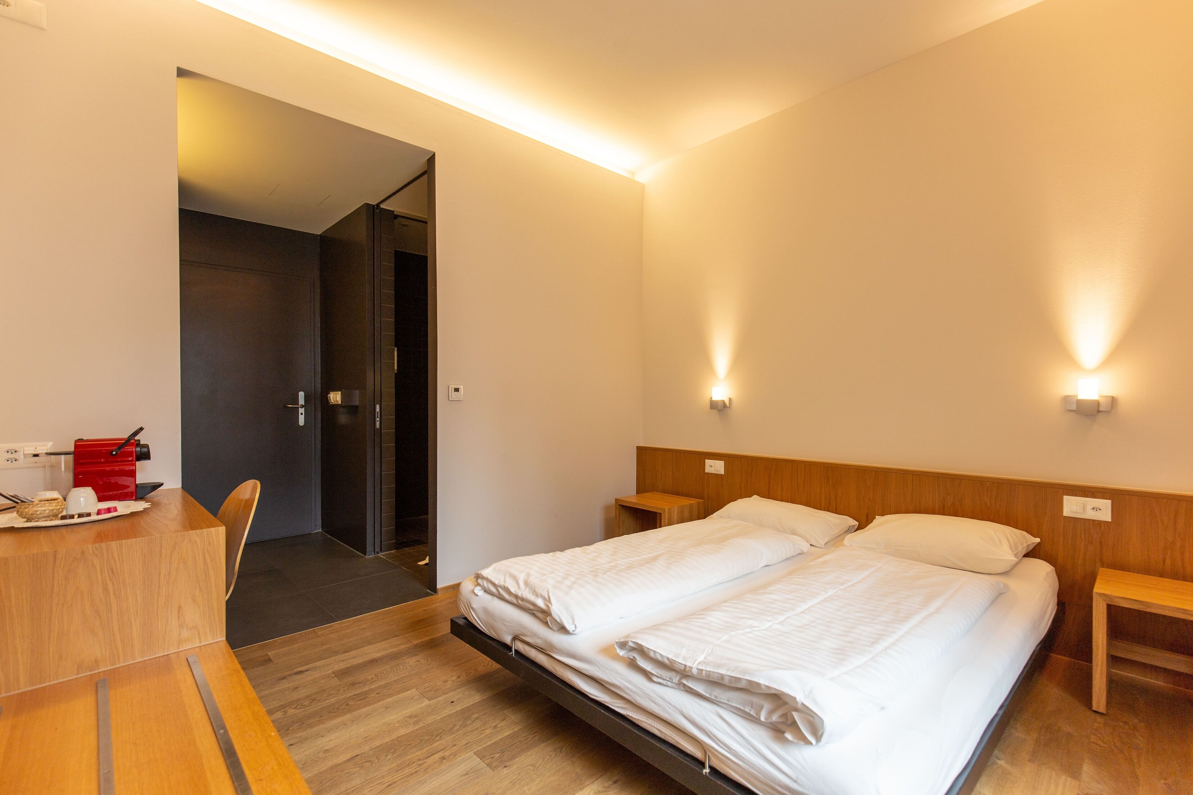 Habitación de hotel con cama, mesitas de noche, escritorio con silla y puerta que da a otra habitación.