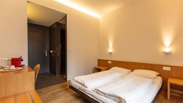 Habitación de hotel con cama, mesitas de noche, escritorio con silla y puerta que da a otra habitación.
