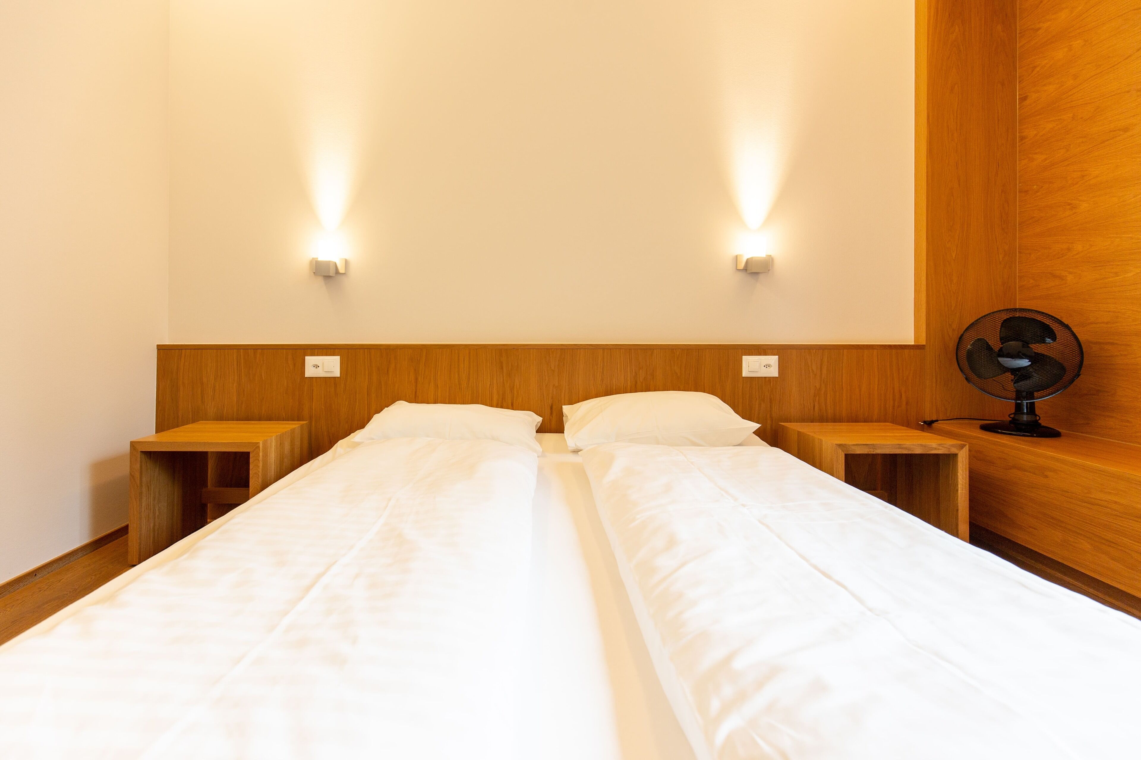A double bed with two wooden nightstands, each with a small shelf and a wall-mounted light.