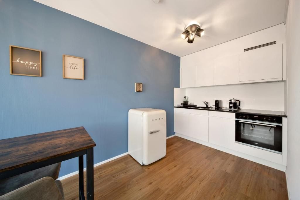 Una cocina compacta con armarios blancos, horno empotrado y refrigerador blanco.
