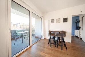 A modern interior with a dining area, a sliding glass door to a balcony, and a kitchenette. - Hyve Hotel Basel - Hostel (Basel)