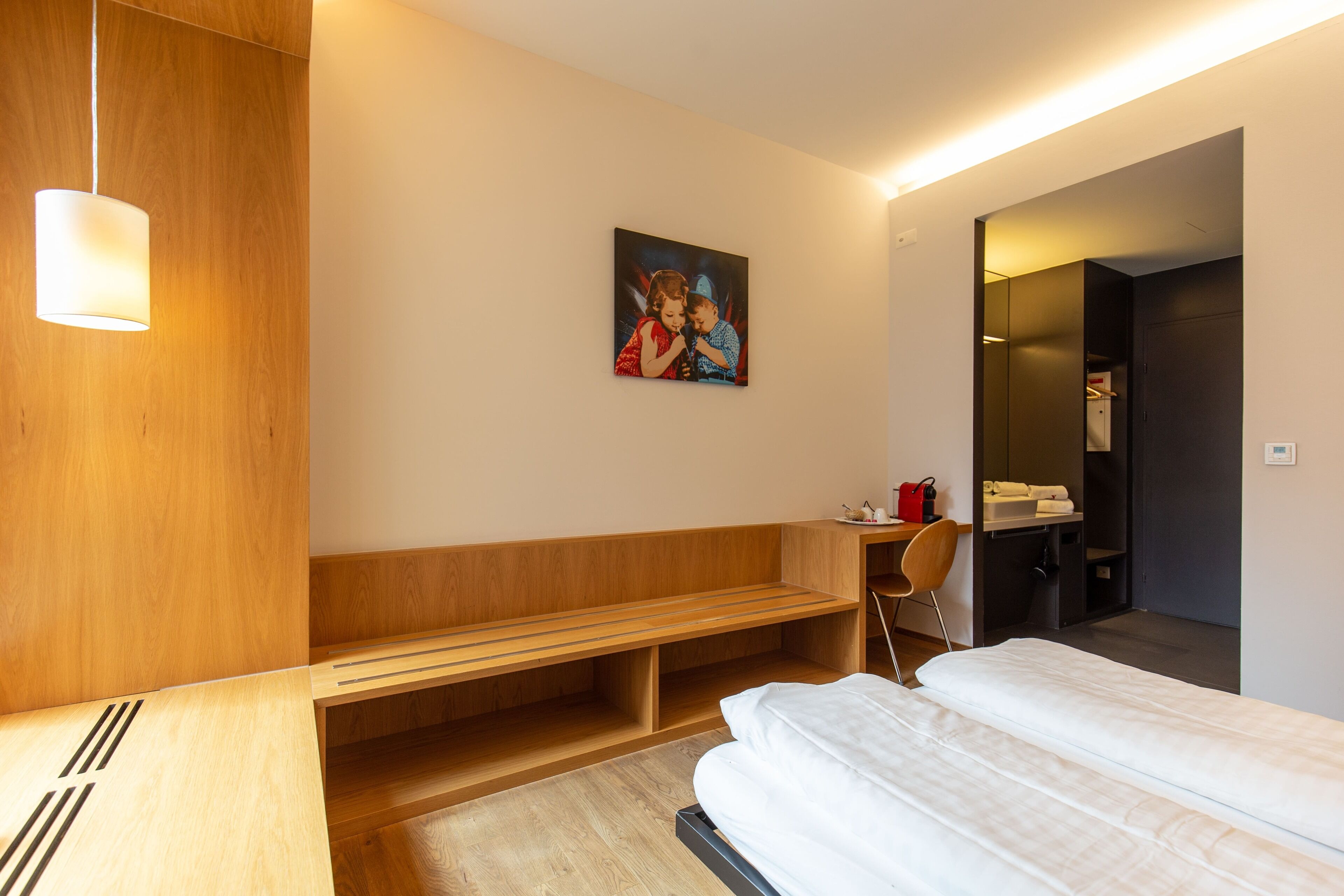 Quarto de hotel moderno com um banco de madeira, uma cama, uma escrivaninha e um quadro na parede.