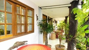 A corridor with wooden-framed windows, potted plants, and a red circular seating area. - Ruan Mai Sang Ngam Resort (Sa Khu)