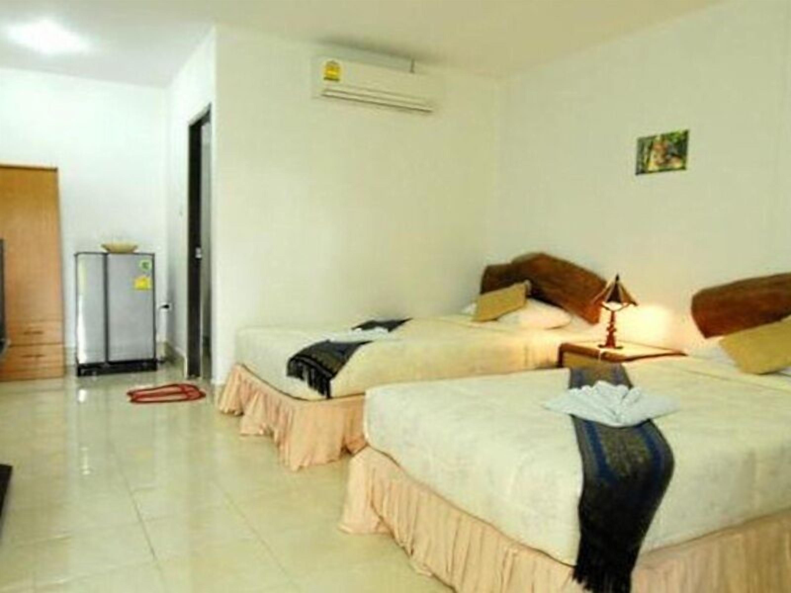 A hotel room with two beds, a small table with a lamp, a refrigerator, and a door leading to another room.