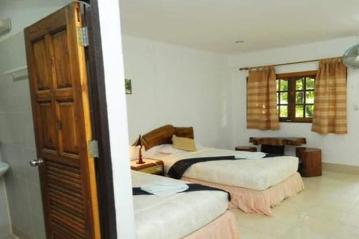 A room with two beds, a window with curtains, a wooden door, and a small table.