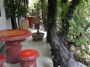 A room with a round wooden table and matching stools, surrounded by potted plants and a large tree trunk.