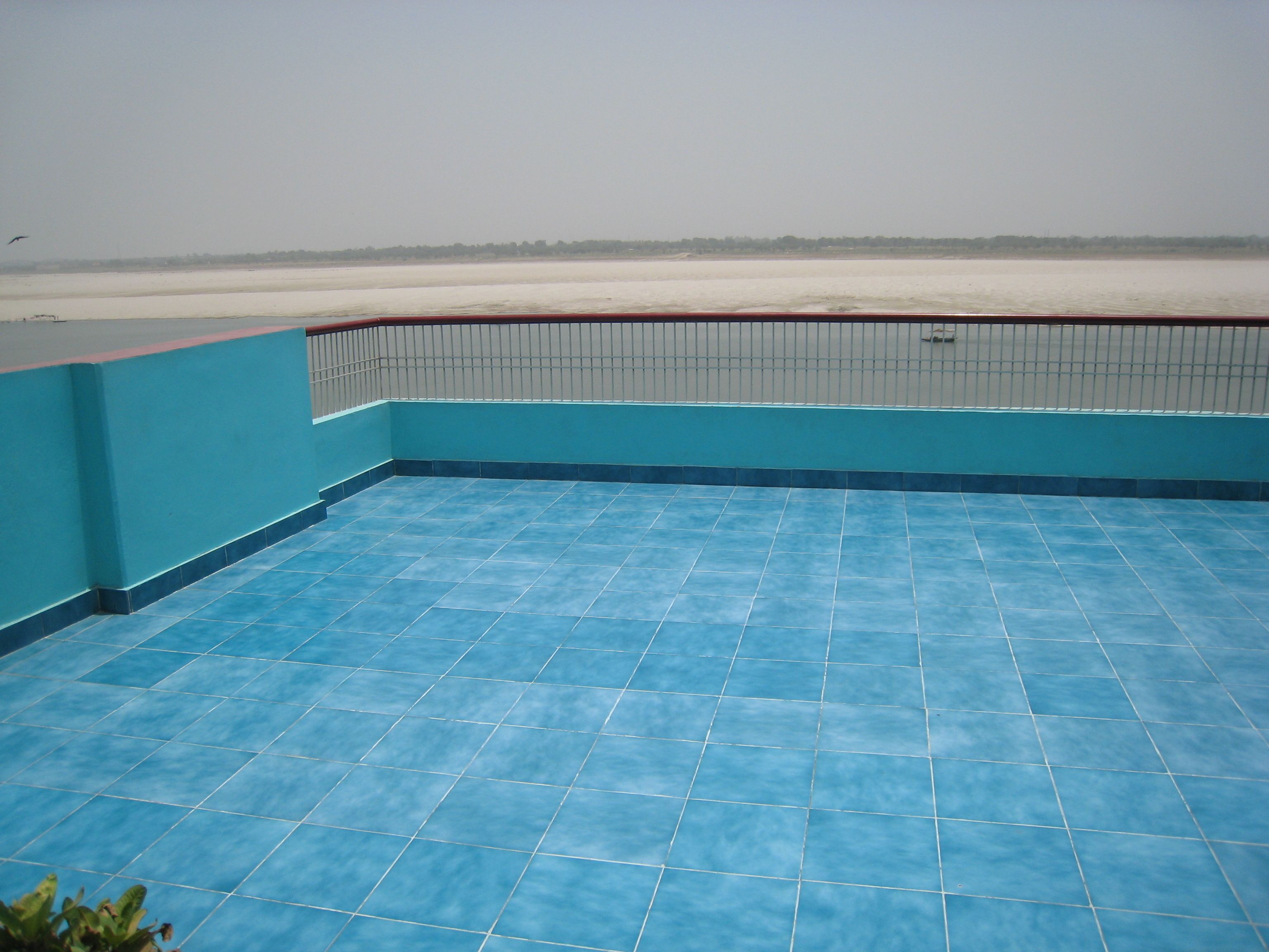 A blue-tiled balcony with a metal railing, overlooking a flat landscape.