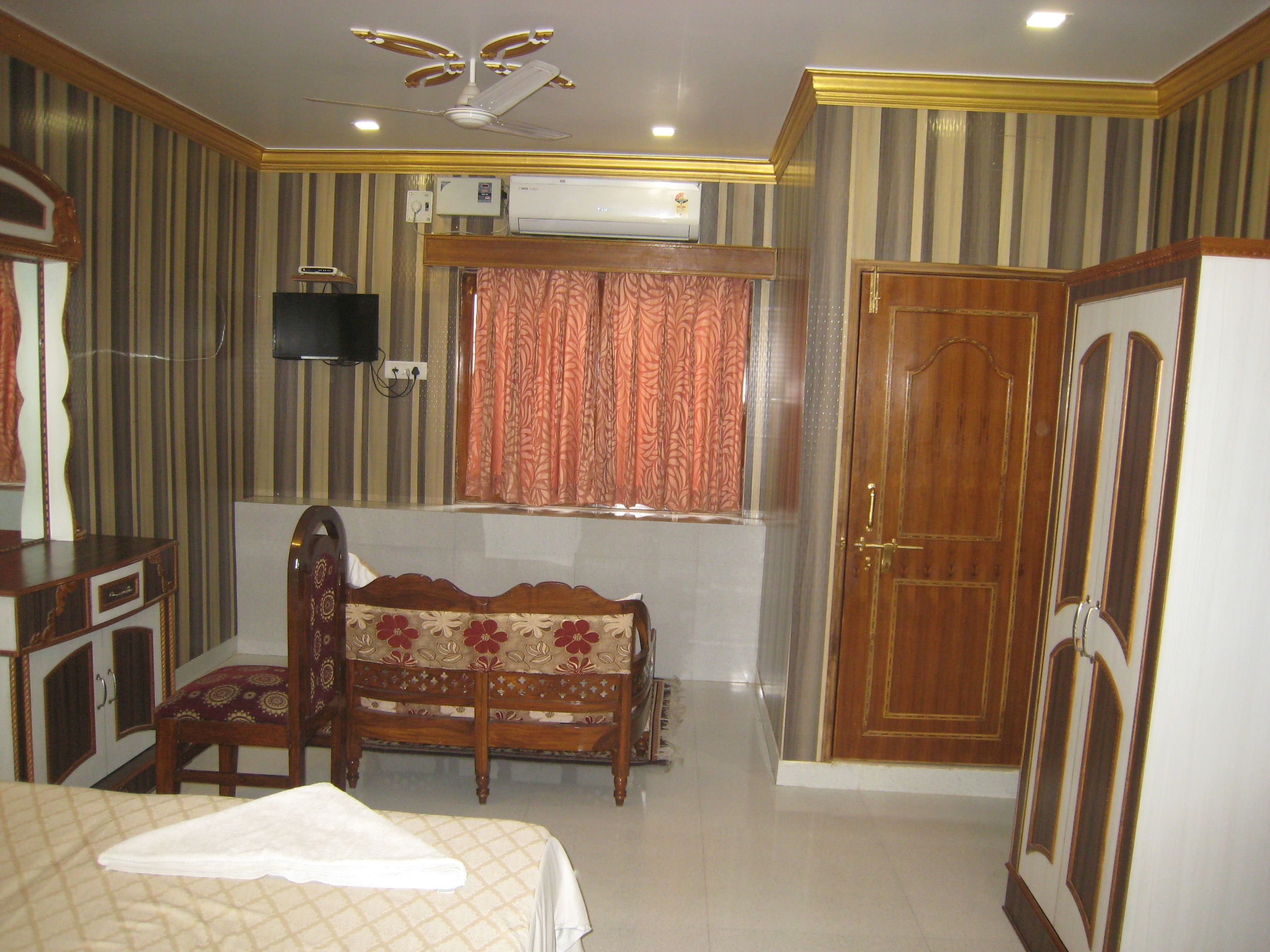 A hotel room with a bed, a wooden chair, a desk, a television, and a wardrobe.