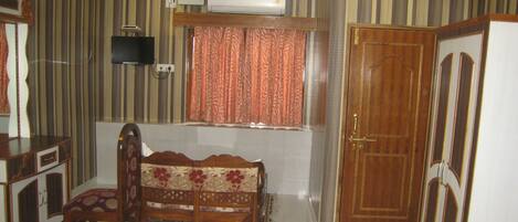 A hotel room with a bed, a wooden chair, a desk, a television, and a wardrobe.