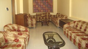 A living room with floral-patterned sofas, a glass coffee table, and a ceiling fan. - Kedareswar Bed and Breakfast (Varanasi)