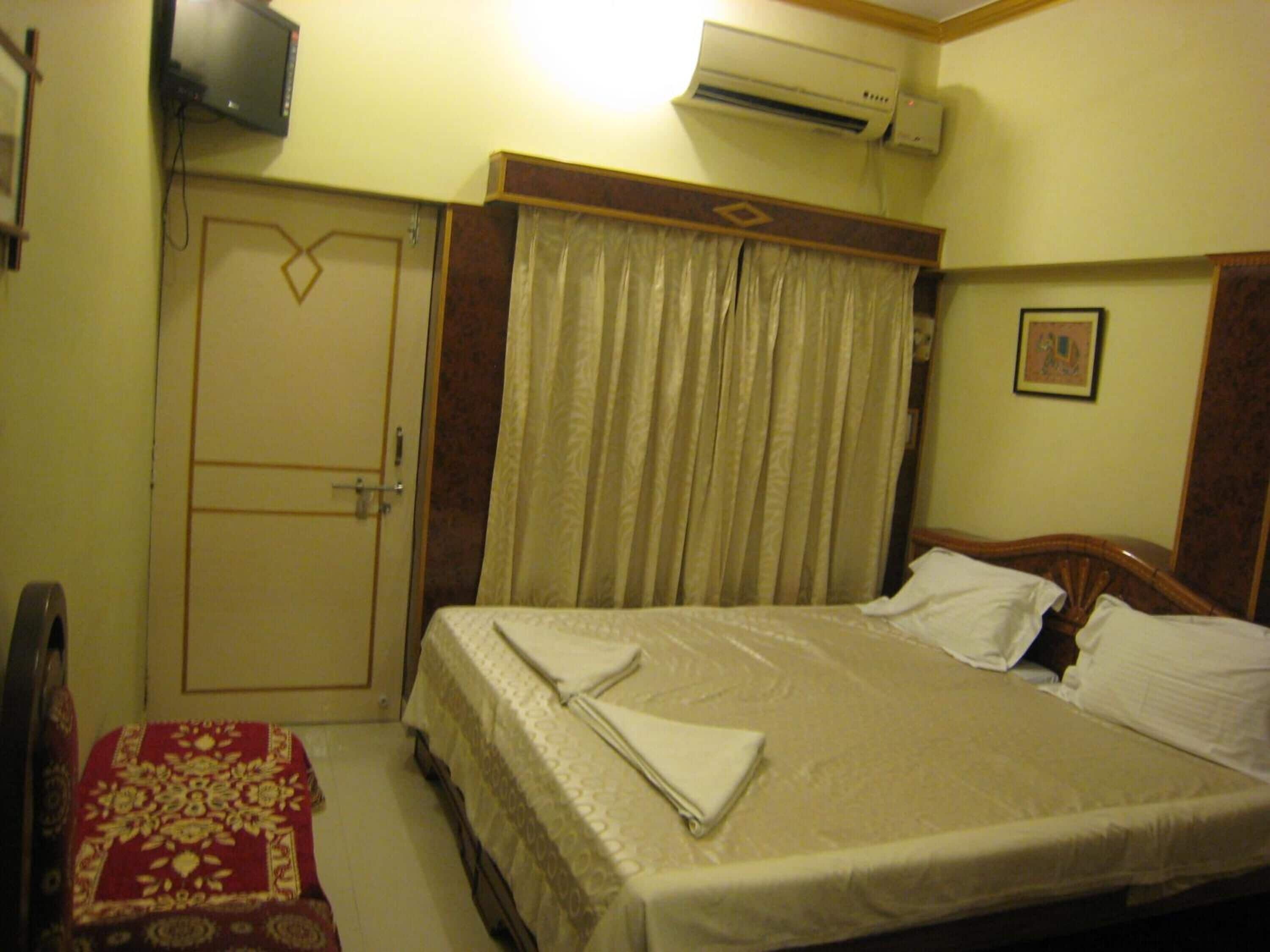 A hotel room with a bed, a TV, an air conditioner, and a door.