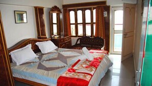 A bedroom with a bed, a dresser, a mirror, and a window with curtains. - Kedareswar Bed and Breakfast (Varanasi)