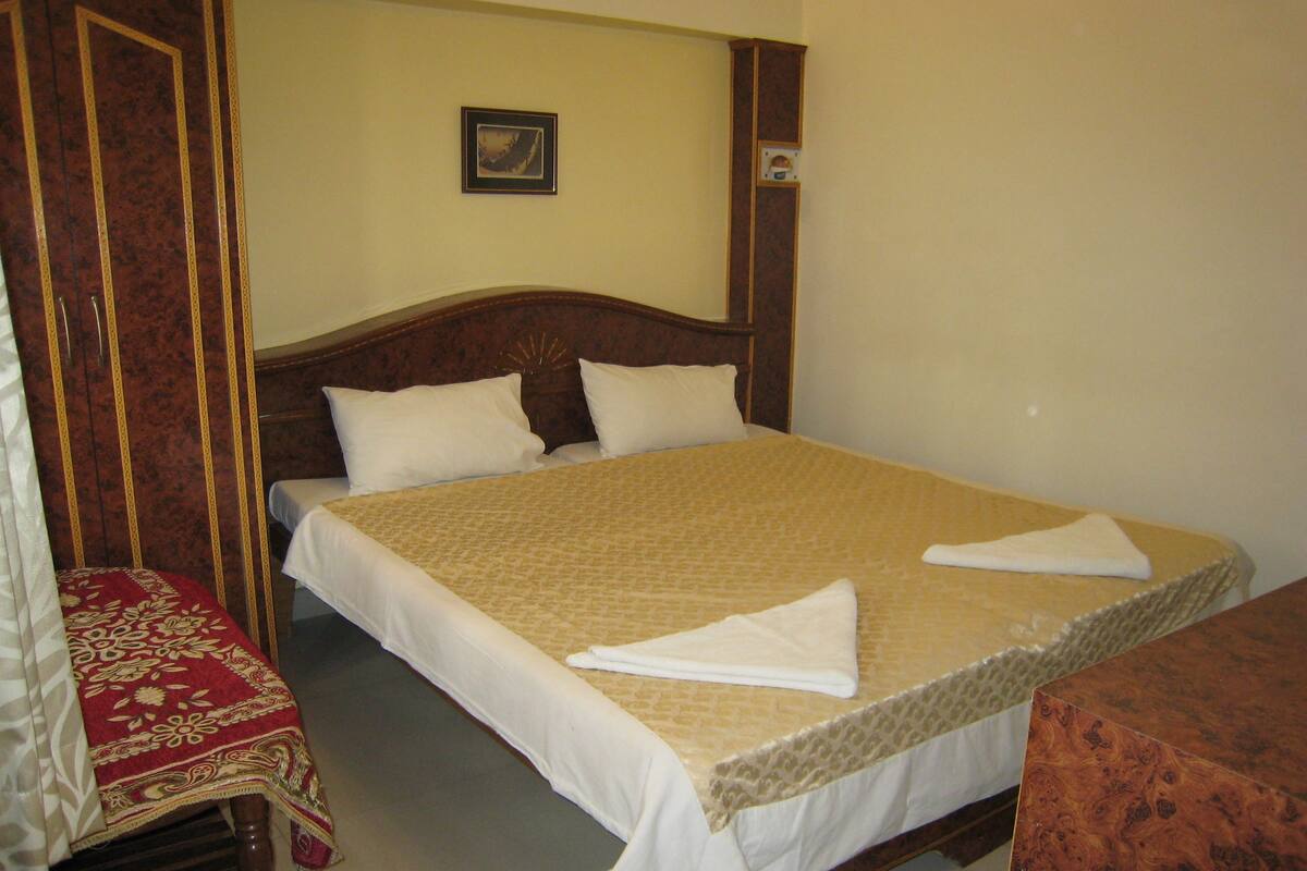A neatly made bed with white linens and a beige bedspread, a wooden headboard, and a small framed picture on the wall.