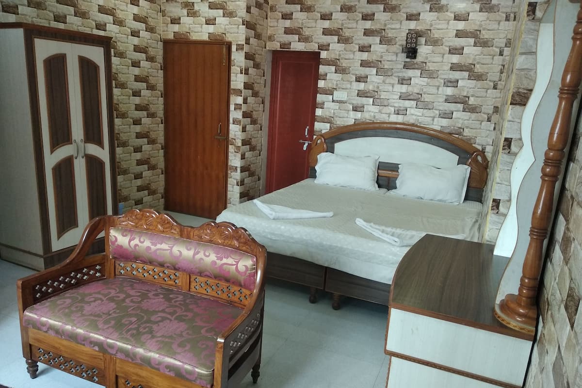 A bedroom with a bed, wooden wardrobe, and a cushioned chair.