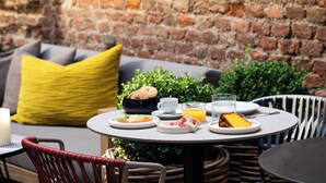A round table with breakfast items, a yellow pillow, and a brick wall in the background. - Residenza dell'Opera (Turin)