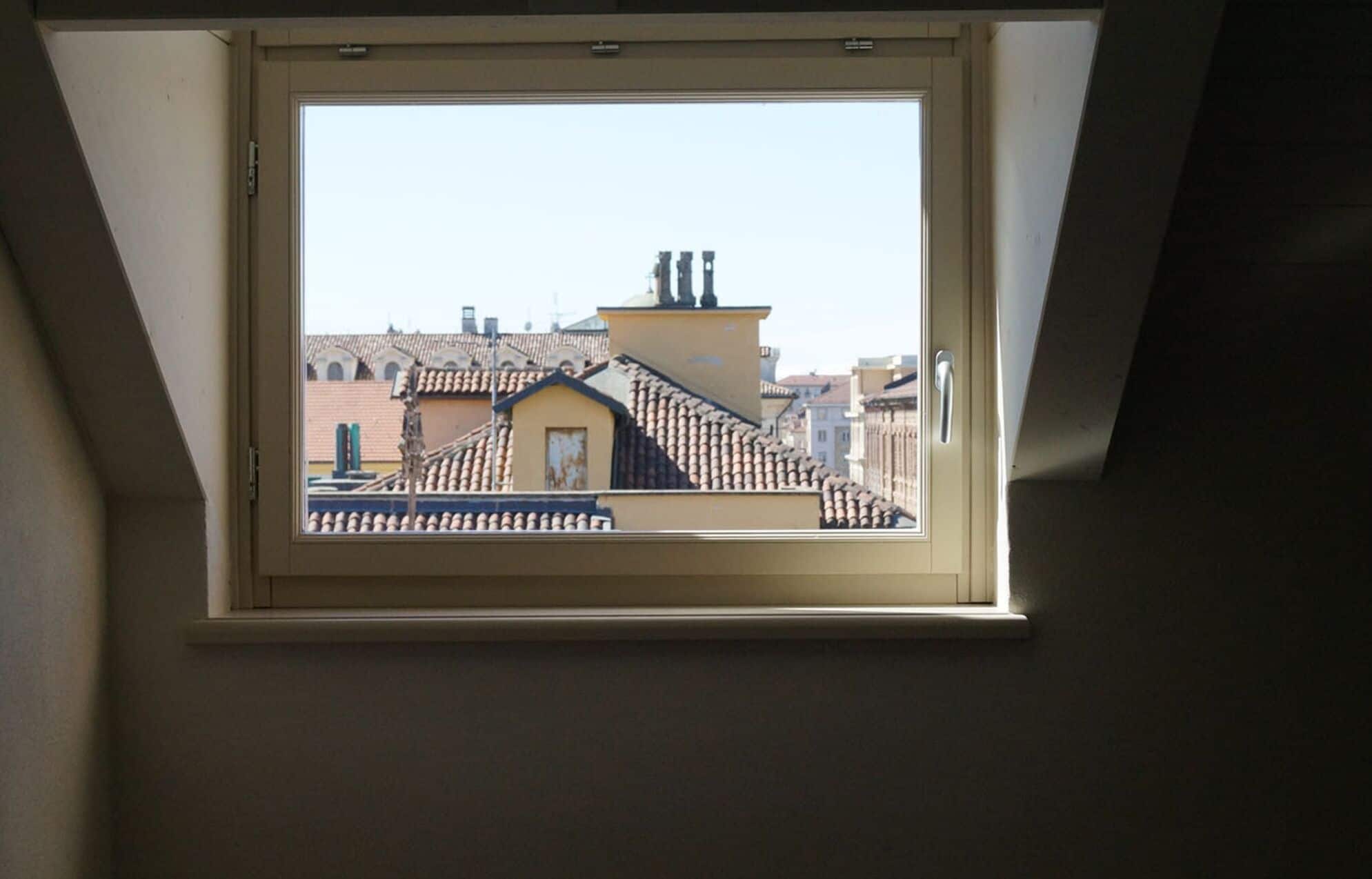 A skylight window with a view of a building's roof and chimney.